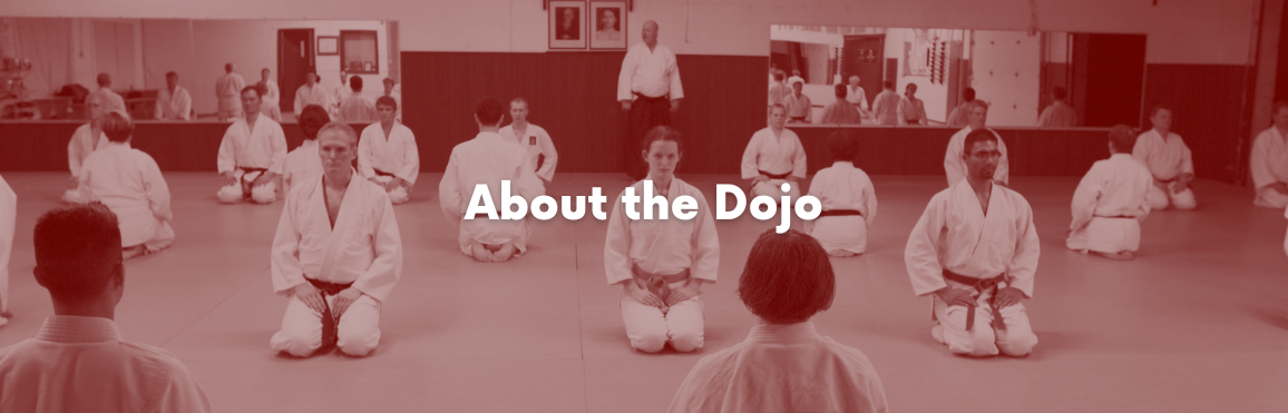 White text that reads “About the Dojo“ overlaid on a photo of people participating in an aikido class. 