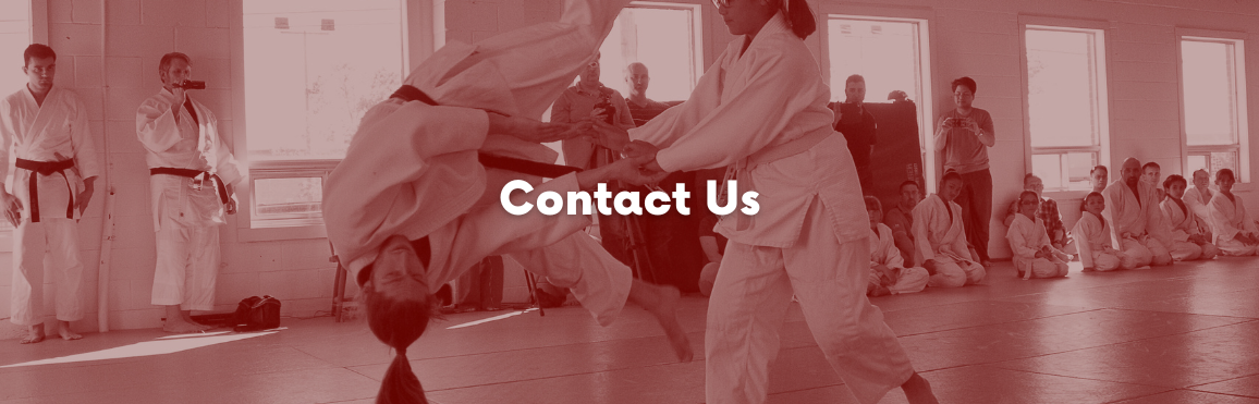 White text that reads “Contact Us“ overlaid on a photo of people participating in an aikido class. 